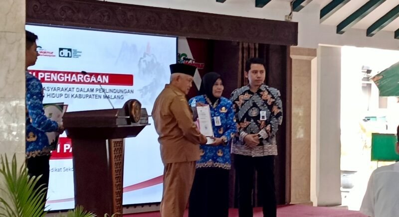 Ket foto. Bupati Malang H.M Sanusi didampingi Plt Kepala Dinas Lingkungan hidup saat menyerahkan  penghargaan lingkungan hidup pada Kepala Sekolah SMPN I Pakis, Dra. Nurus Solehati